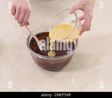 Making Brownies, pouring egg mixture into melted chocolate and mixing in Stock Photo