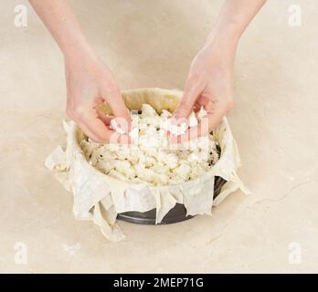 Making Feta Filo Pie, sprinkling feta cheese over spinach mixture in pastry case Stock Photo