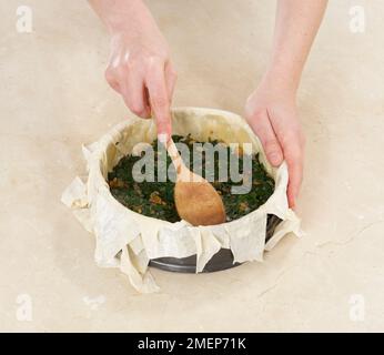 Making Feta Filo Pie, spreading spinach mixture in pastry case Stock Photo