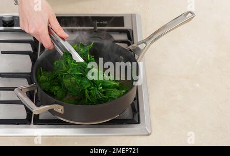 Cooking spinach in pan, turning over occasionally, until just wilted, to make filling for feta filo pie Stock Photo