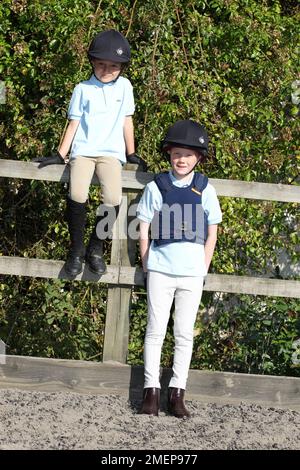 Young girl and boy wearing riding habit sitting and leaning against fence, front view Stock Photo