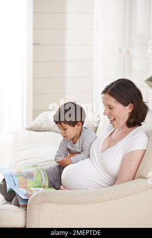 Pregnant woman sitting on sofa reading to small boy Stock Photo