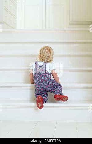 Girl crawling up stairs, 18 months Stock Photo