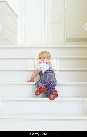 Girl crawling up stairs, 18 months Stock Photo