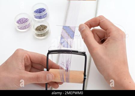 Making a loom-woven bead cuff, adding new weft thread with needle, close-up Stock Photo