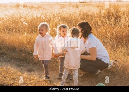 Mom on walk with daughters triplets. One girl is crying. Kids tantrums at street. Upset baby boy at park. Childhood. Stock Photo