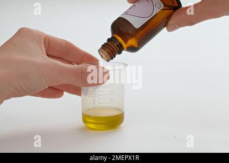 Measuring fragrance poured from bottle into small measuring beaker, close-up Stock Photo