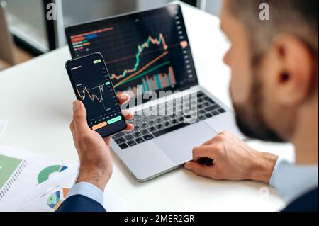 Trader investor analyst using mobile phone app for cryptocurrency stock market, analyzing graph trading data index investment growth chart, plans strategy. Close-up of male hands holding smartphone Stock Photo