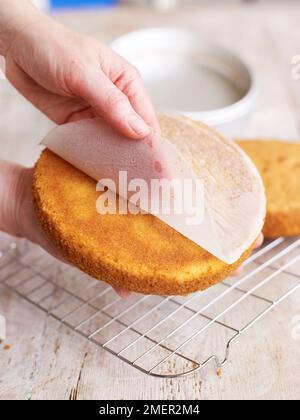 Peeling off lining paper from Victoria sponge cake base Stock Photo