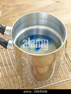 Blue dye dissolving in water at bottom of double-boiler (making candles) Stock Photo