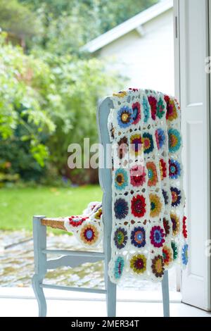 Colourful, flower-pattern crochet blanket hanging over chair back Stock Photo