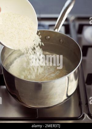 Adding rice to pan of boiling water Stock Photo