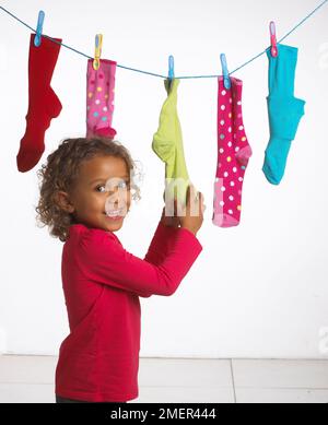 Girl holding sock in a row of colourful socks on washing line, 4 years Stock Photo