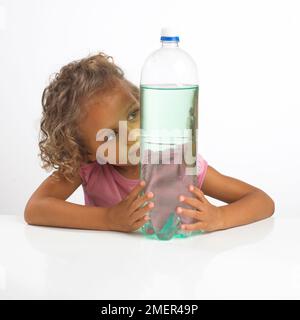 Girl looking at reflection in large bottle of water, 4 years Stock Photo