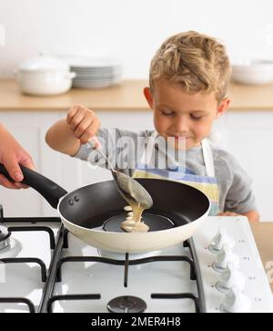 Boy spooning pancake mixture into frying pan, 4 years Stock Photo