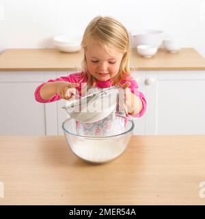 Girl sieving flour into a bowl, 3 years Stock Photo