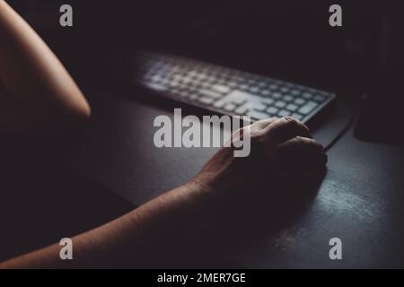 Woman using desktop computer mouse in dark home office interior, closeup of hands with selective focus Stock Photo