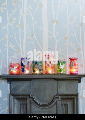 Candle glass jars decorated with tissue paper flowers and silver pendants, on mantelpiece Stock Photo