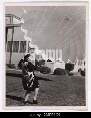 Photograph of Spar Opan Jean Evans. A new SPAR reporting at the U.S. Coast Guard Air Station, San Diego, California finds out about a parachute. Representative of many SPARs who are replacing men on shore jobs is Evans, Opal Jean, Sea.2c., pictured here, who has been assigned a job number as a truck driver. Stock Photo