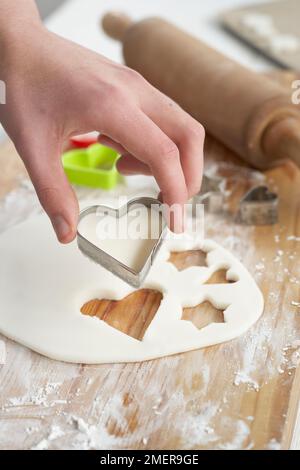 Cutting heart shape from bicarbonate of sofa and corn flour dough, making pendants Stock Photo