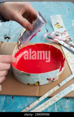 Attaching strips of covered card to outside edge of plate using strong glue, making paper birdcage Stock Photo