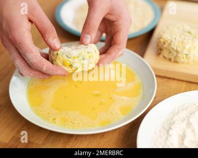 Dipping uncooked fish cakes in beaten egg Stock Photo