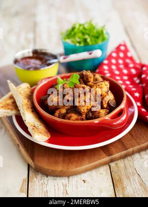 Roasted marinated chicken pieces served in red bowl with pitta bread Stock Photo
