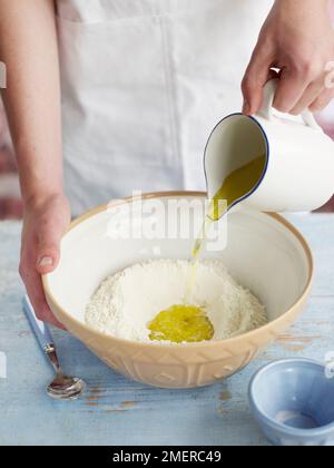 Pouring olive oil and water into flour well, making focaccia bread Stock Photo