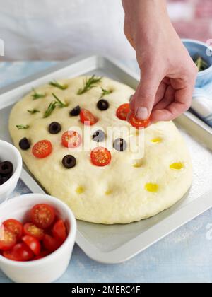 Studding focaccia bread with rosemary, olives and cherry tomatoes, olive oil Stock Photo
