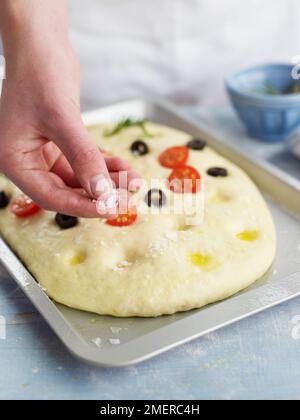 Studding focaccia bread with olives and cherry tomatoes and adding salt Stock Photo