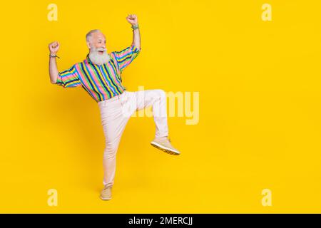 Full length photo of positive funky guy dressed striped shirt looking empty space rising fists isolated yellow color background Stock Photo