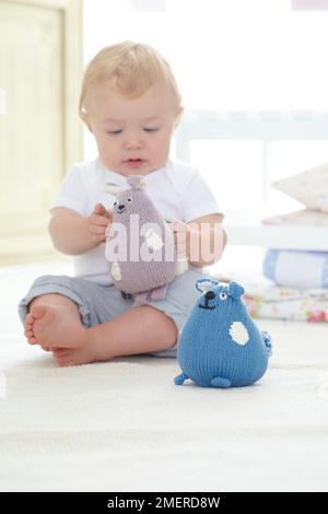 Baby boy sitting holding soft knitted animal toys, 10 months Stock Photo