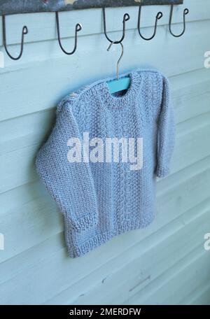 Knitted jumper hanging on coat hanger from clothes hook Stock Photo