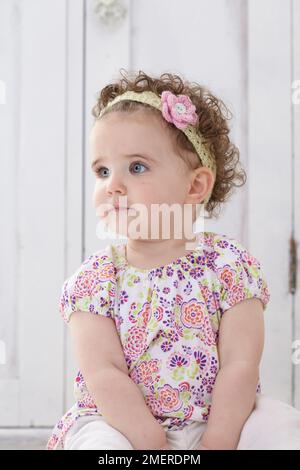 Baby girl sitting wearing knitted headband, 14 months Stock Photo