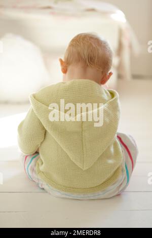 Baby girl wearing knitted hoodie sitting on the floor, 17 months Stock Photo