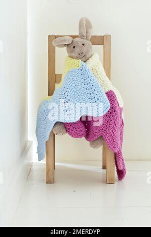 Toy bunny wrapped in colourful knitted blanket Stock Photo