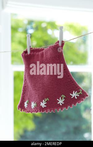 Knitted baby's skirt with daisy detail hanging from washing line Stock Photo