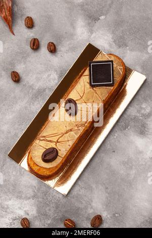 Eclair with coffee flavoured cream filling and chocolate on golden cardboard Stock Photo