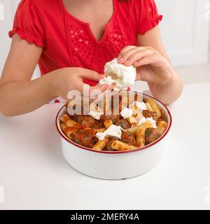 Girl breaking up mozzarella cheese to place on pasta bake Stock Photo