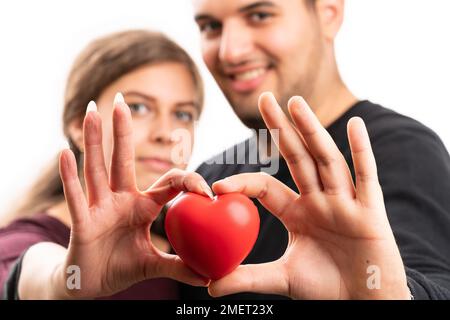 Close-up with selective focus of red heart held presented by cute girlfriend and boyfriend couple as romantic love concept isolated on white studio ba Stock Photo