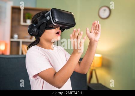 excited girl kid with wow experience while using Vr or virtual reality headset feeling objects by trying to touch in the air on metaverse - concept of Stock Photo