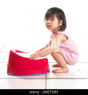 Girl crouching wearing pink vest holding a red potty, 20 months Stock Photo