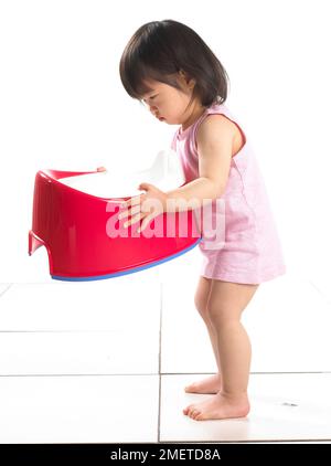 Girl standing wearing pink vest holding a red potty, 20 months Stock Photo