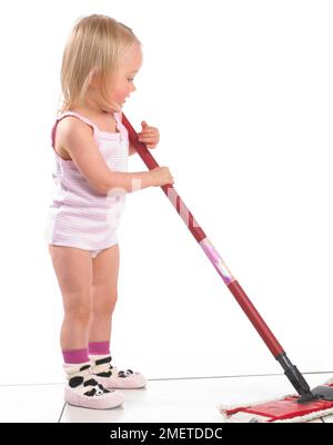 Girl wearing vest, pants and slippers using a mop, 20 months Stock Photo