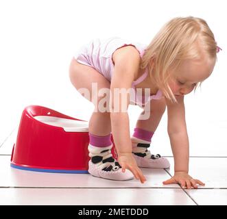 Girl wearing vest and slippers standing up from a potty, 20 months Stock Photo