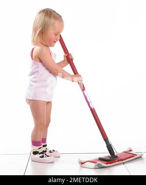 Girl wearing vest, pants and slippers using a mop, 20 months Stock Photo