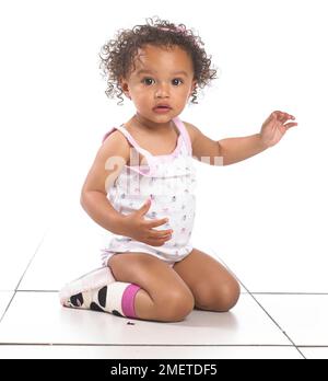 Girl wearing vest, pants and slippers, kneeling, 16 months Stock Photo