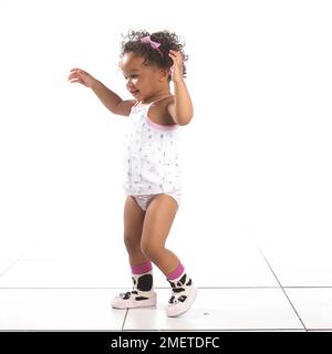 Girl wearing pants, vest and slippers standing with arms in the air, 16 months Stock Photo