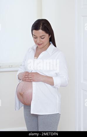 Heavily pregnant woman with her belly exposed, holding soft toy Stock