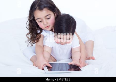 Baby girl (40 weeks) and her older sister (3.5 years) looking at tablet computer together Stock Photo